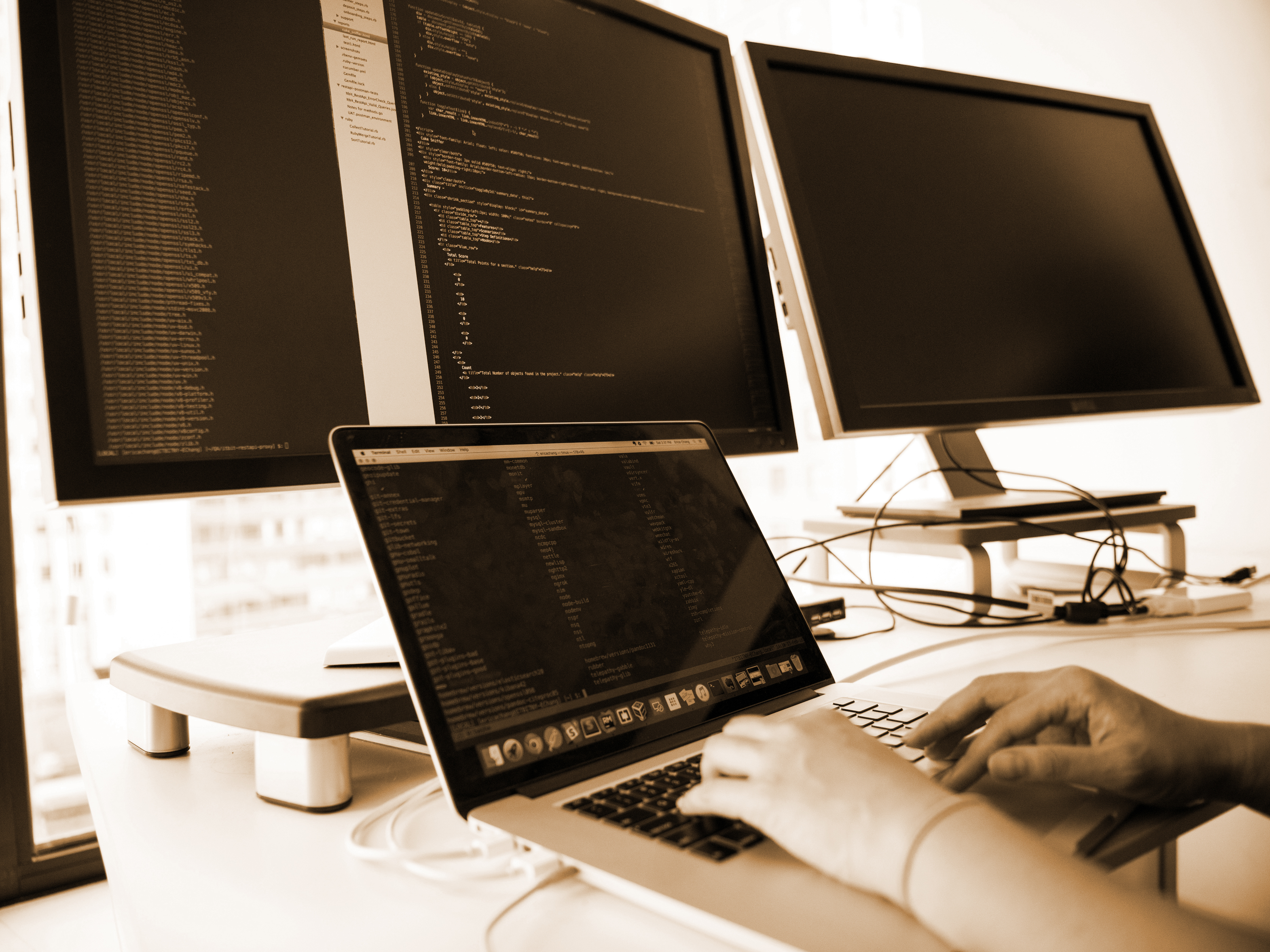 A workspace with 3 monitors and someone typing on a laptop.